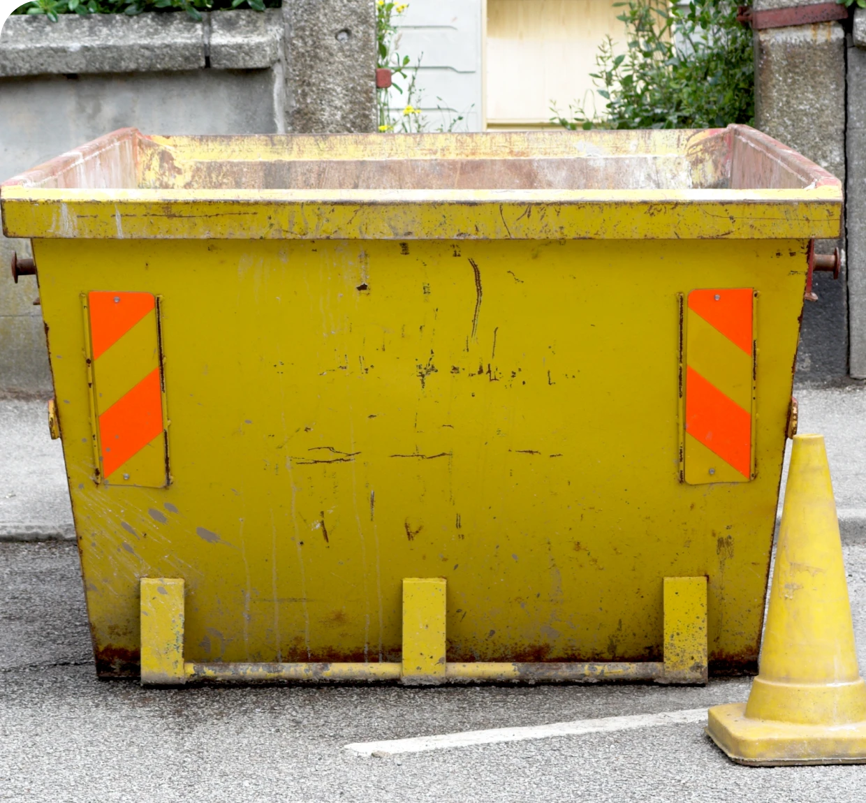 Empty yellow dumpster beside traffic cone